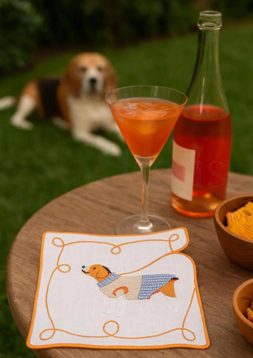 Linen cocktail napkin with an embroidered dog beside an orange cocktail